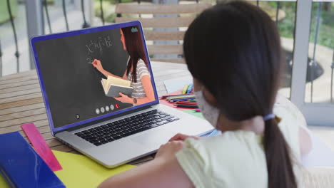 estudiante caucásica con máscara facial usando una computadora portátil en una videollamada con una maestra