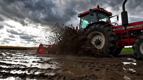 red tractor plowing muddy field under dramatic sky
