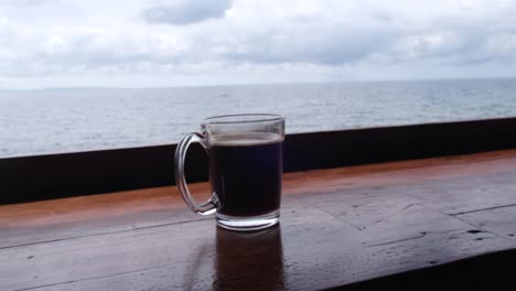 Frisch-Gebrühter-Schwarzer-Kaffee-In-Einem-Becher-Mit-Ruhiger-Meereslandschaft-Im-Hintergrund