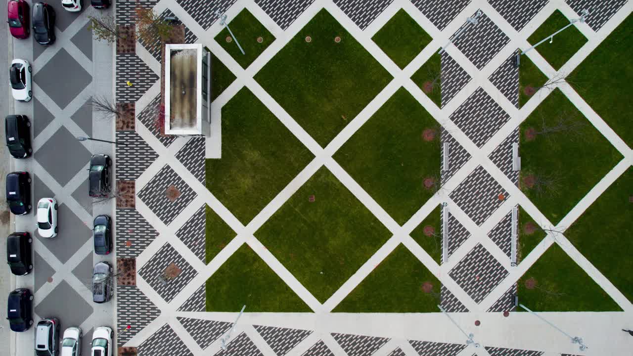 Top-down view of Paved plaza with contemporary geometric brick patterns, road with cars, woonerf, and people walking