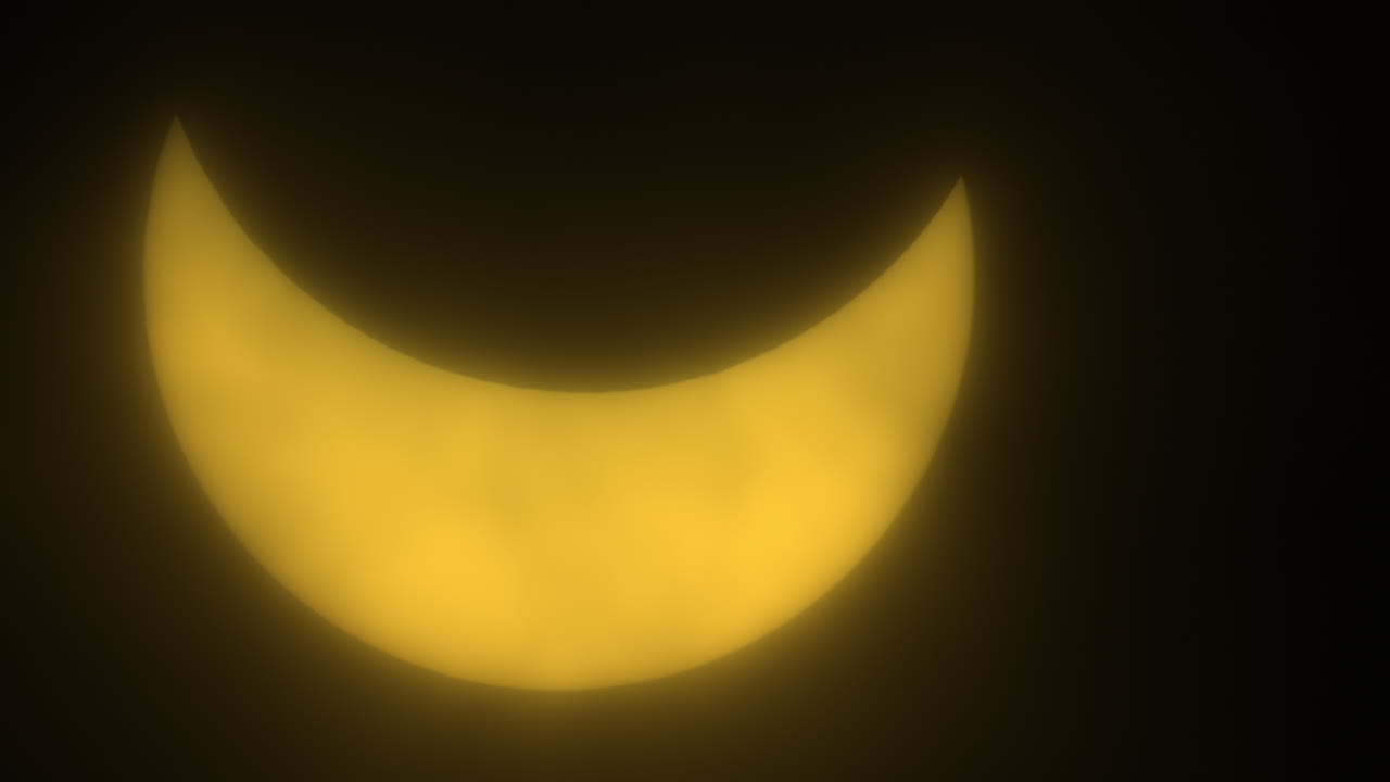 Sun Glowing Yellow Behind Passing Clouds During Partial Eclipse