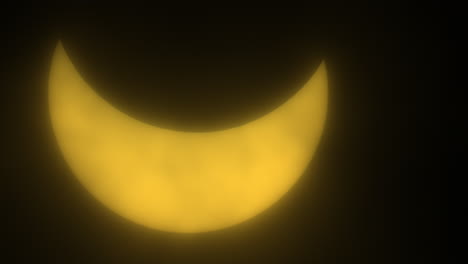 sun glowing yellow behind passing clouds during partial eclipse