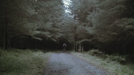 Youth-cycles-down-forest-pathway-within-nature-wearing-backpack