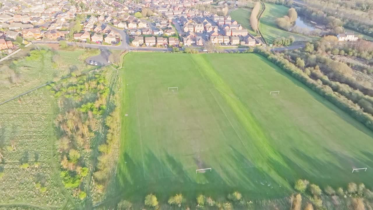 Smooth aerial drone push-in reveals a large green football pitch with multiple goalposts, bordered by trees and adjacent to a suburban neighborhood in Wombwell, Barnsley, South Yorkshire, England
