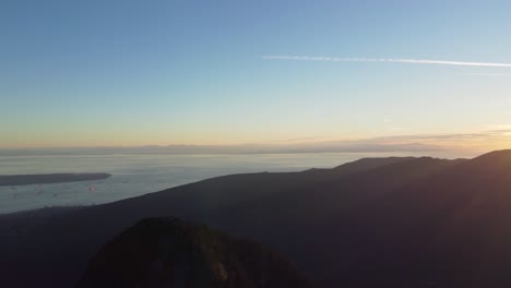 Panorámica-De-Drones-Al-Atardecer-Brillante-Sobre-El-Paisaje-Montañoso-Con-El-Océano-Y-La-Ciudad-De-Vancouver