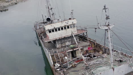 Rusty-grey-half-submerged-shipwreck-anchored-near-the-shore-on-a-cloudy-overcast-day