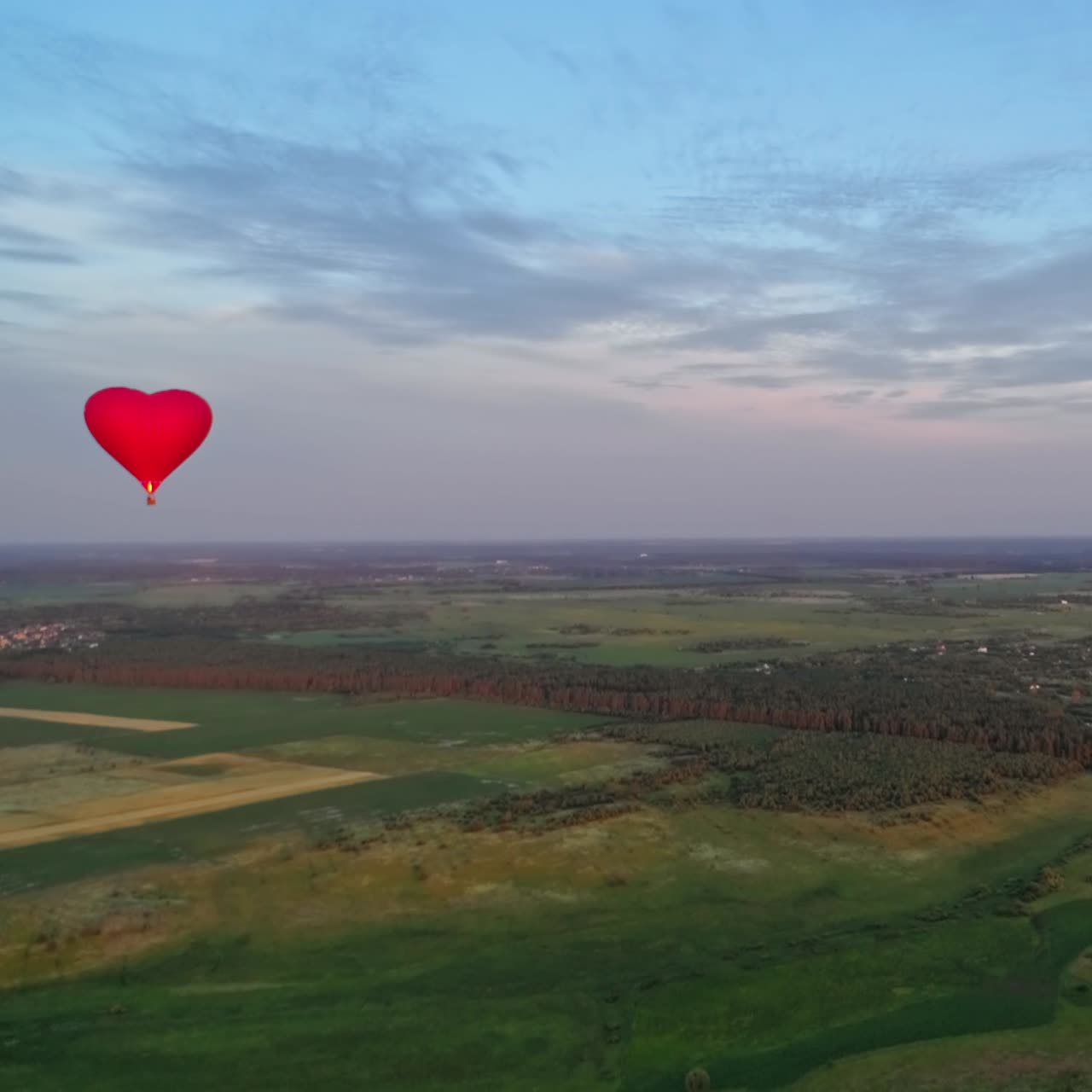 Summer landscape and aerostat in the air. Red hot air balloon flying over the green fields against the beautiful sky.