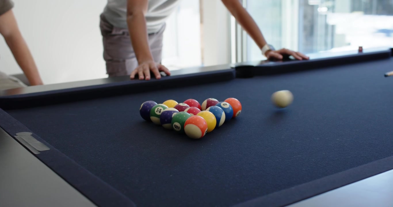 Male friends playing pool at home, left friend breaking balls, center friend watching and gesturing