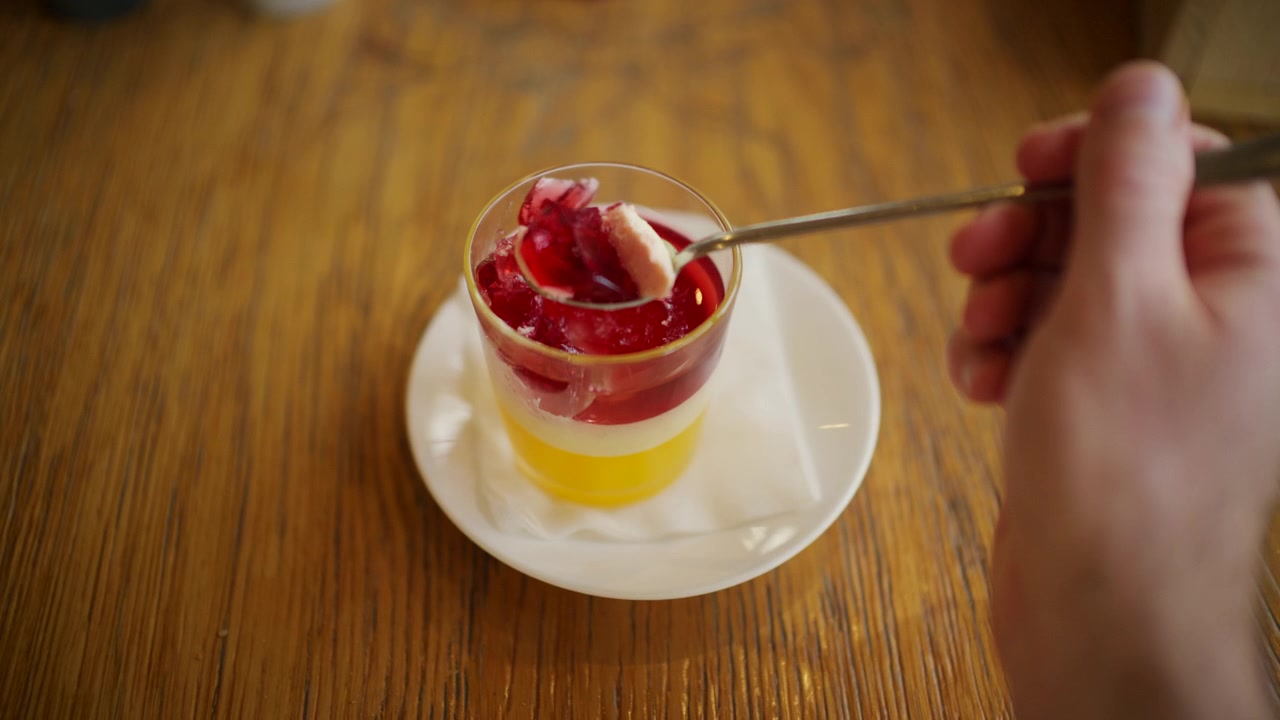 Primo piano di un cucchiaio che solleva un pezzo di gelatina di frutta rosso vivo da una coppetta da dessert di plastica trasparente.