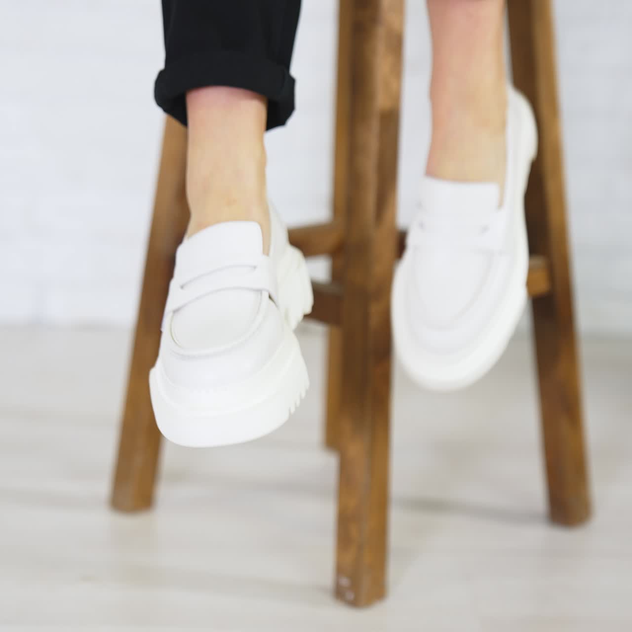 Presentation of white shoes with plain massive soles. Lady in modern footwear sits on the tabouret waving her feet. Close up