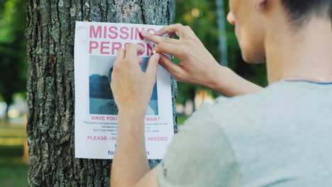 un joven pone anuncios de una persona desaparecida en el parque