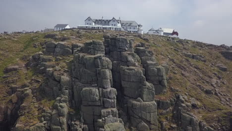 Rotating-aerial-of-rugged-sea-cliffs-and-hotel,-Lands-End,-Cornwall-UK