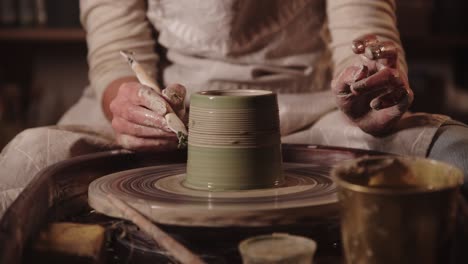 young woman potter making bridges on the wet pot using a tool