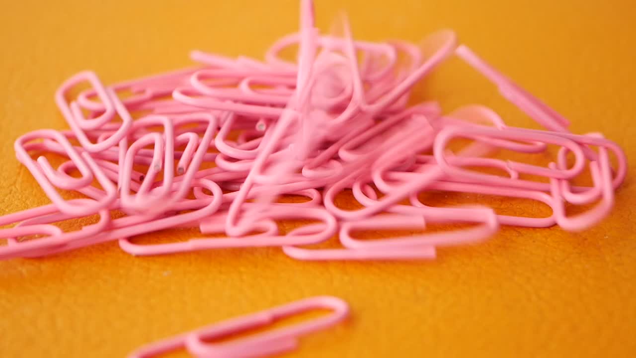 Pile of pink paperclips on orange surface