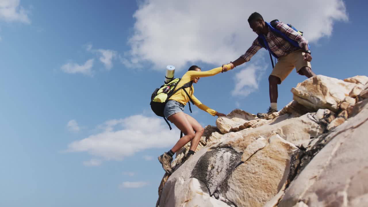 pareja afroamericana subiendo a las rocas mientras hacen trekking