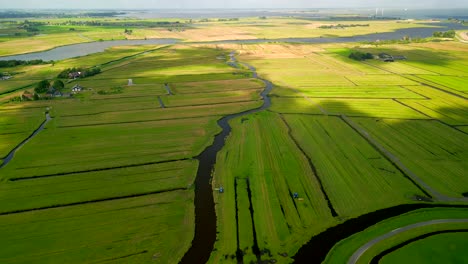 aerial drone footage of a polder landscape with green pastures in the netherlands on a sunny, partially cloudy day.