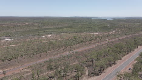 Toma-Aérea-De-Drones-En-Movimiento-De-La-Carretera-Y-El-Ferrocarril-Con-La-Ciudad-De-Darwin-En-La-Distancia-En-El-Territorio-Del-Norte,-Interior-Australiano