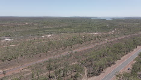 aerial moving drone shot of highway and railway with darwin city in the distance in northern territory, australian outback
