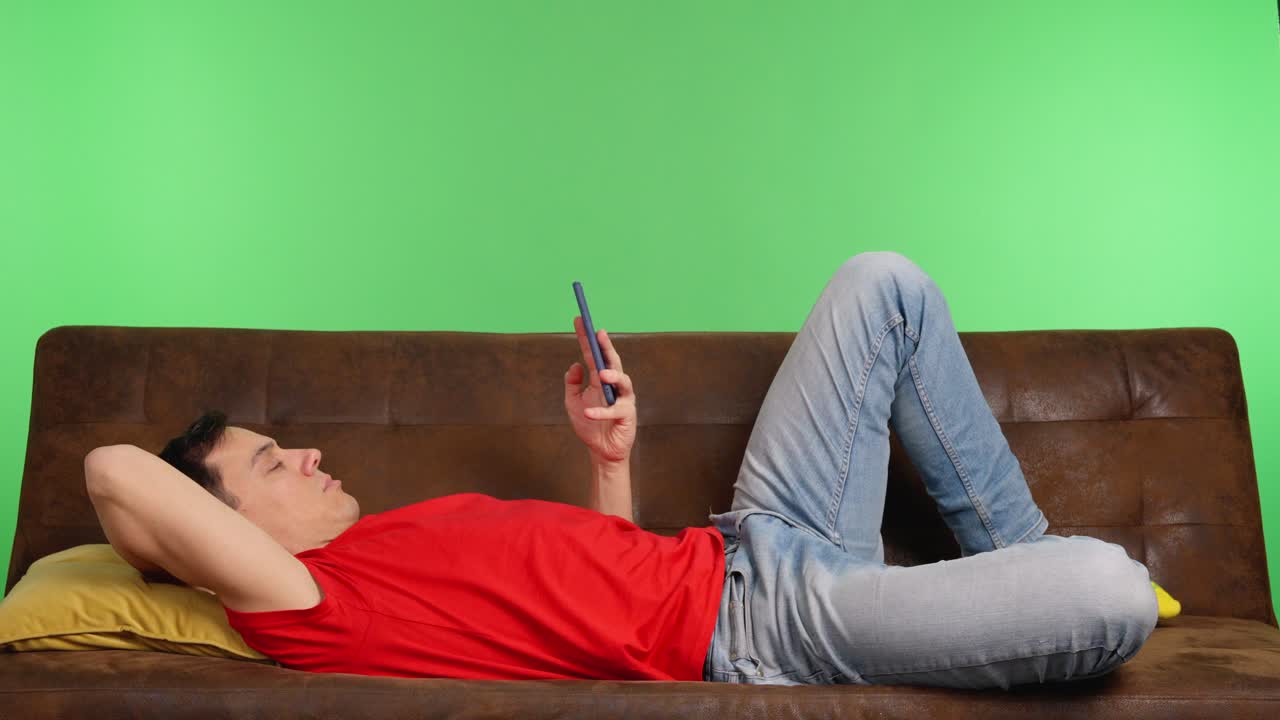 Man relaxing on sofa using smartphone with green screen
