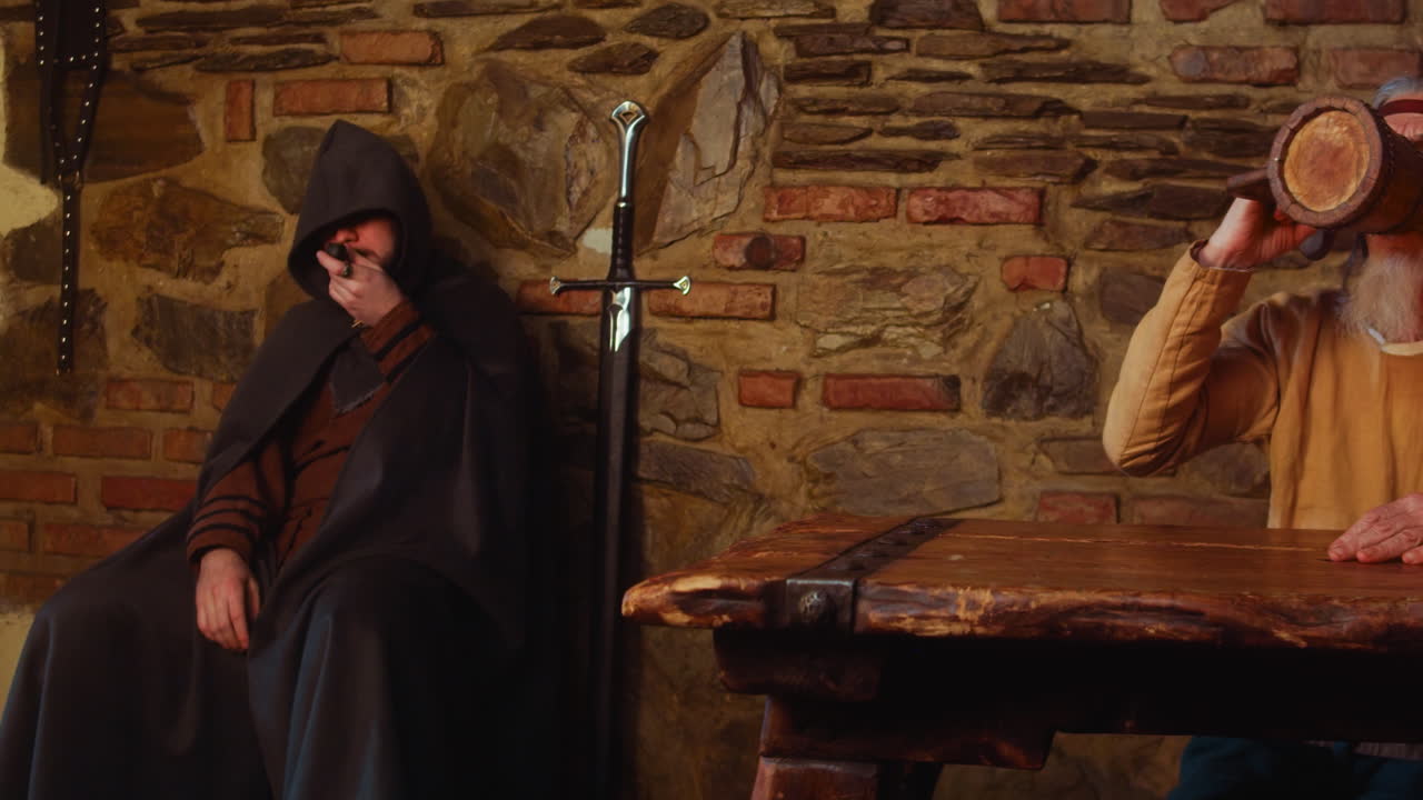People rest and servant works in medieval tavern. Stranger with pipe old man and thief in hood and young waitress in pub. Historical role play performance