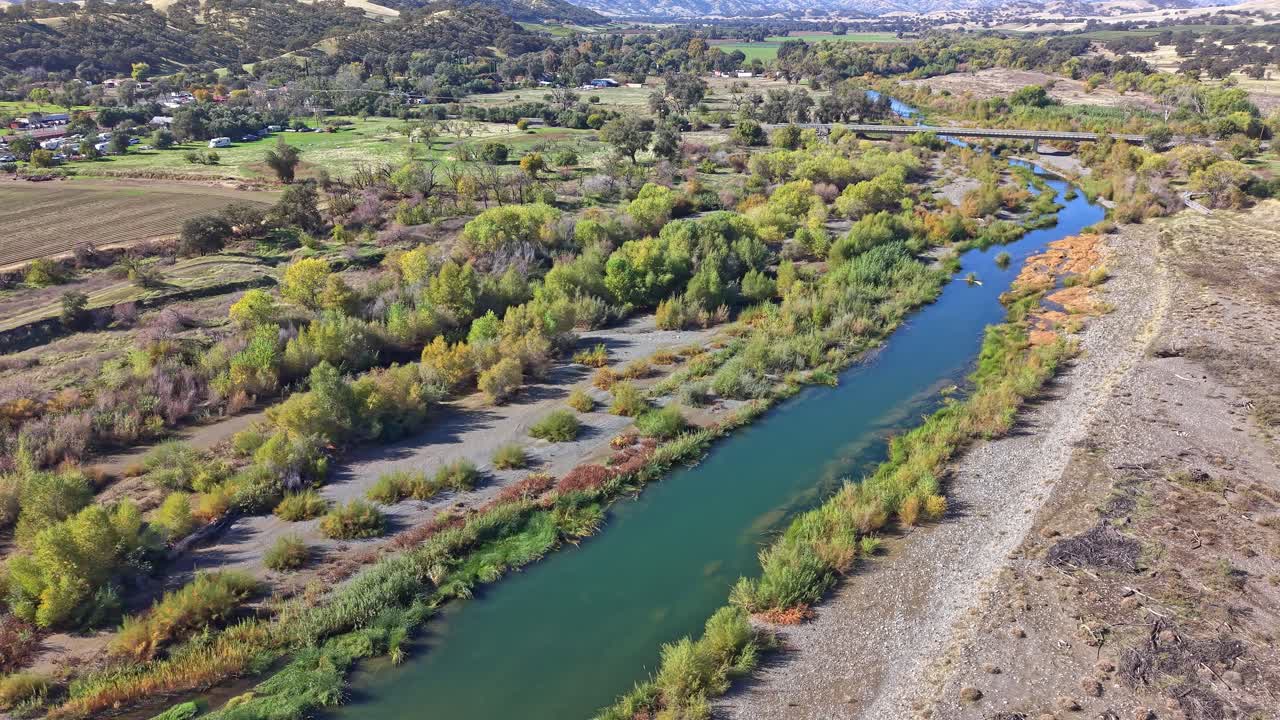 Drone arcs in a panning motion, then tilts to align with Cache Creek before stabilizing above the river and dense vegetation in Capay, California