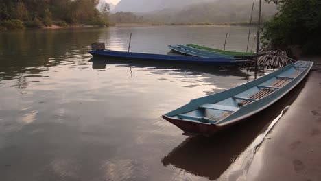 wooden-boats-docked-on-riverside-in-the-mountain-town-of-Nong-Khiaw-in-Laos,-Southeast-Asia