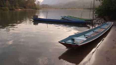 barcos de madera atracados a la orilla del río en la ciudad montañosa de nong khiaw en laos, sudeste asiático