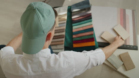 A-young-designer-chooses-finishing-materials-for-repair-and-stylish-interior,-he-has-an-album-with-samples-of-fabrics,-wallpaper-and-wood-samples