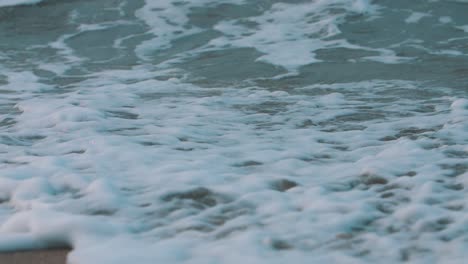 espuma de primer plano de las olas rompiendo en la arena en cámara lenta