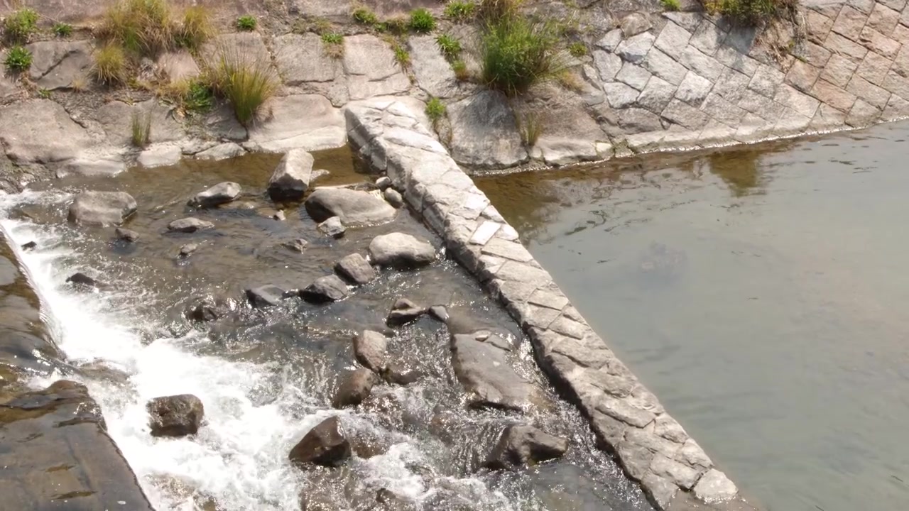 Toma cenital estática de agua fluyendo desde una alcantarilla de hormigón hacia un río rocoso.