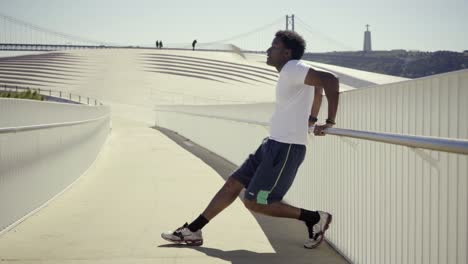 concentrated young man stretching legs near metal railing.