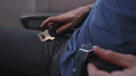 close up on male hands unfastening or unbuckling seatbelt after landing or during flight and getting up from seat