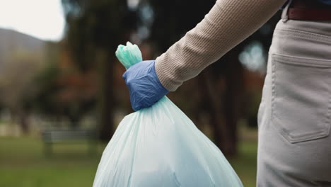 person in blue gloves holding a trash bag in a park