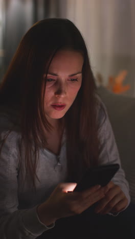 Vertical-Video-Of-Anxious-Woman-Lying-On-Sofa-At-Home-Looking-At-Mobile-Phone-Concerned-About-Social-Media-Or-Bad-News