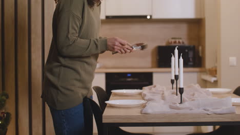 Camera-Focuses-On-Woman-Placing-Cutlery-On-The-Table-Decorated-With-Candles-And-A-Tablecloth-For-Christmas-Dinner