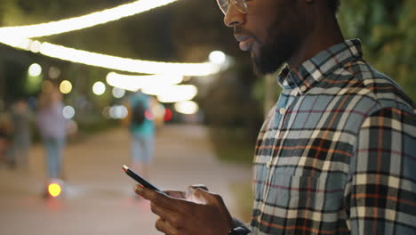 african american man typing on phone in park in evening