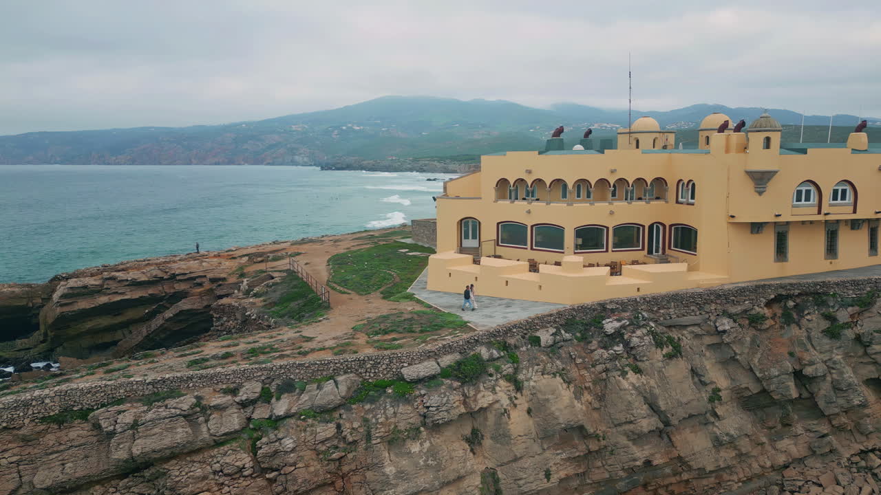 Aerial coastal hotel complex overlooking ocean from rugged cliffs. Rocky beach