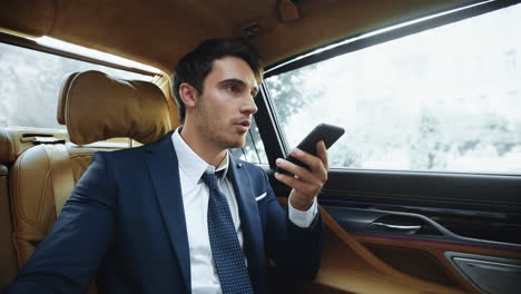 hombre profesional enfocado en la grabación de mensajes de voz a un teléfono inteligente en un coche moderno.