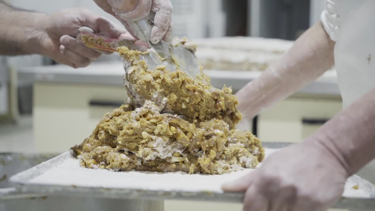 Slow motion panning shot of a dough for candy on a tablet held by a baker while using a spatula to stack more dough