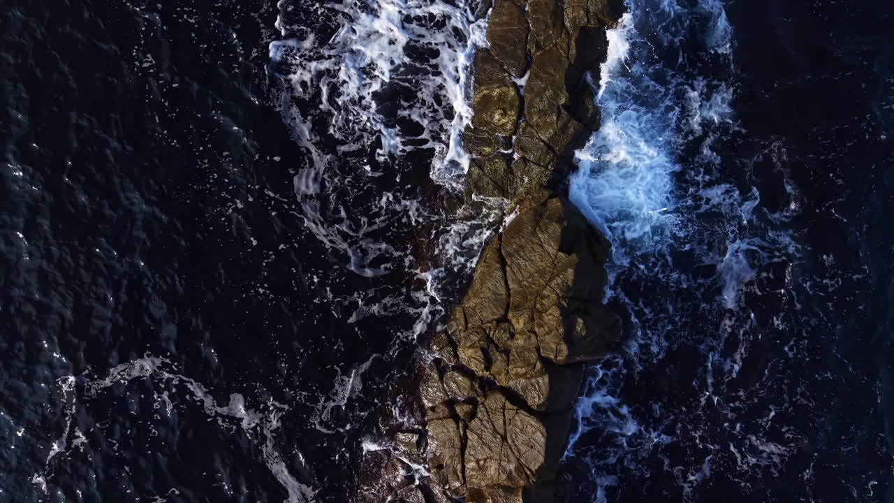 Ocean waves crashing against rugged rocks in a serene coastal landscape at dusk
