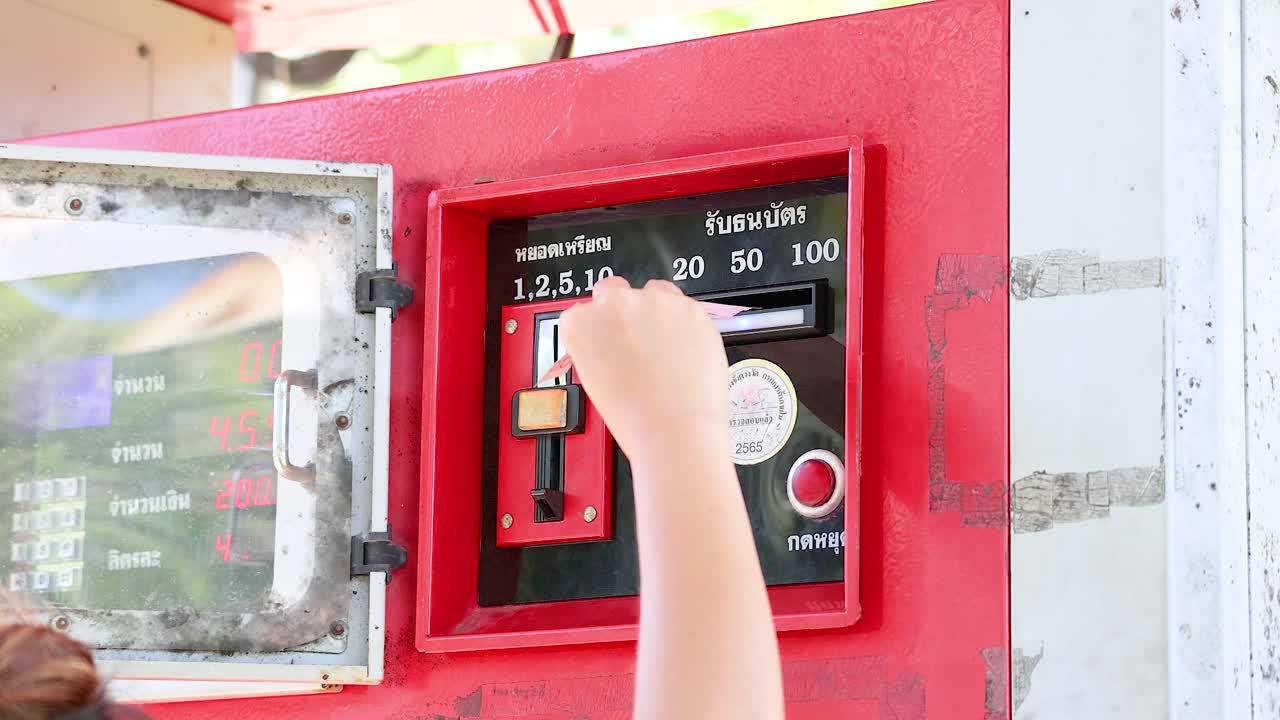 A person inserts cash into a red coin-operated fuel dispenser at Khao Rang Viewpoint, Phuket, under bright daylight