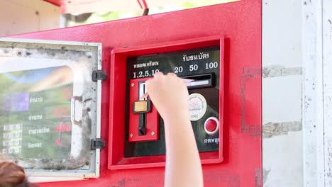 a person inserts cash into a red coin-operated fuel dispenser at khao rang viewpoint, phuket, under bright daylight