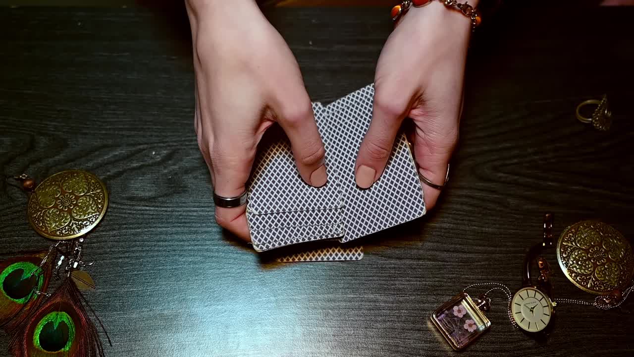 Fortune teller hands collects cards from the table among mysterious bright jewelry. Overhead warm shot. Slow motion