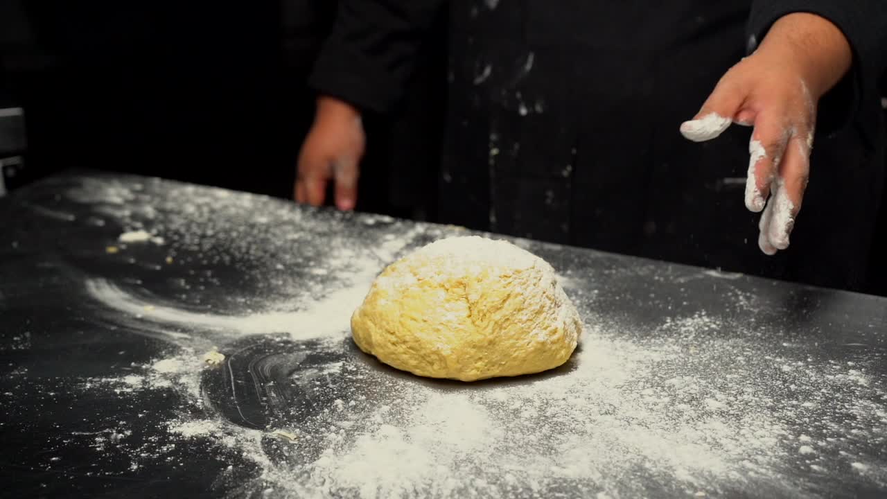 Bäcker streut Mehl über Teig für die Zubereitung von Brot und Hamburgerbrötchen auf einem Küchentisch in einem Gourmetrestaurant