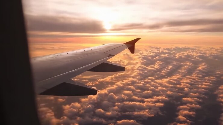 Vue aérienne vidéo depuis la fenêtre d'un avion au coucher du soleil, capturant l'aile au-dessus de nuages duveteux