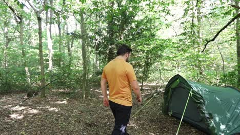 man going to a tent at campsite in the woods and crouches down in front of the entrance