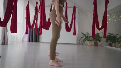downward view of wellness advocates shifting legs and bodies in synchronized flow, inside spacious studio with red aerial hammocks and soft daylight, capturing energy, and mindful coordination