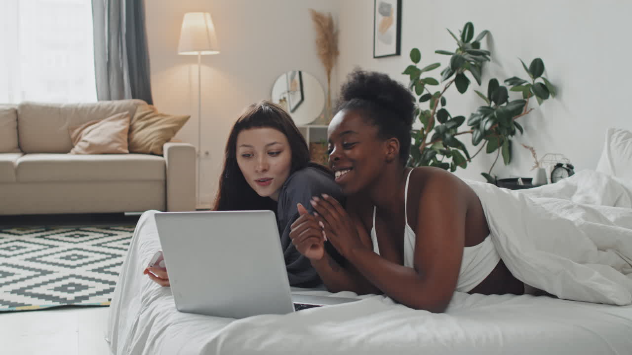 Female Couple Relaxing on Bed and Using Gadgets
