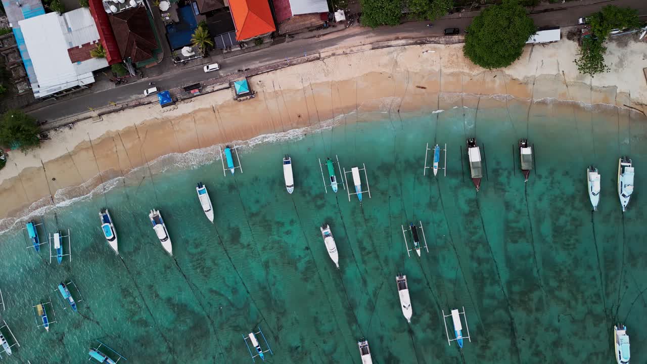 Stunning top down drone view of Padang bai Beach in Bali, where boats rest over turquoise water and golden sand, showcasing the peaceful beauty of this tropical harbor and its coastal charm