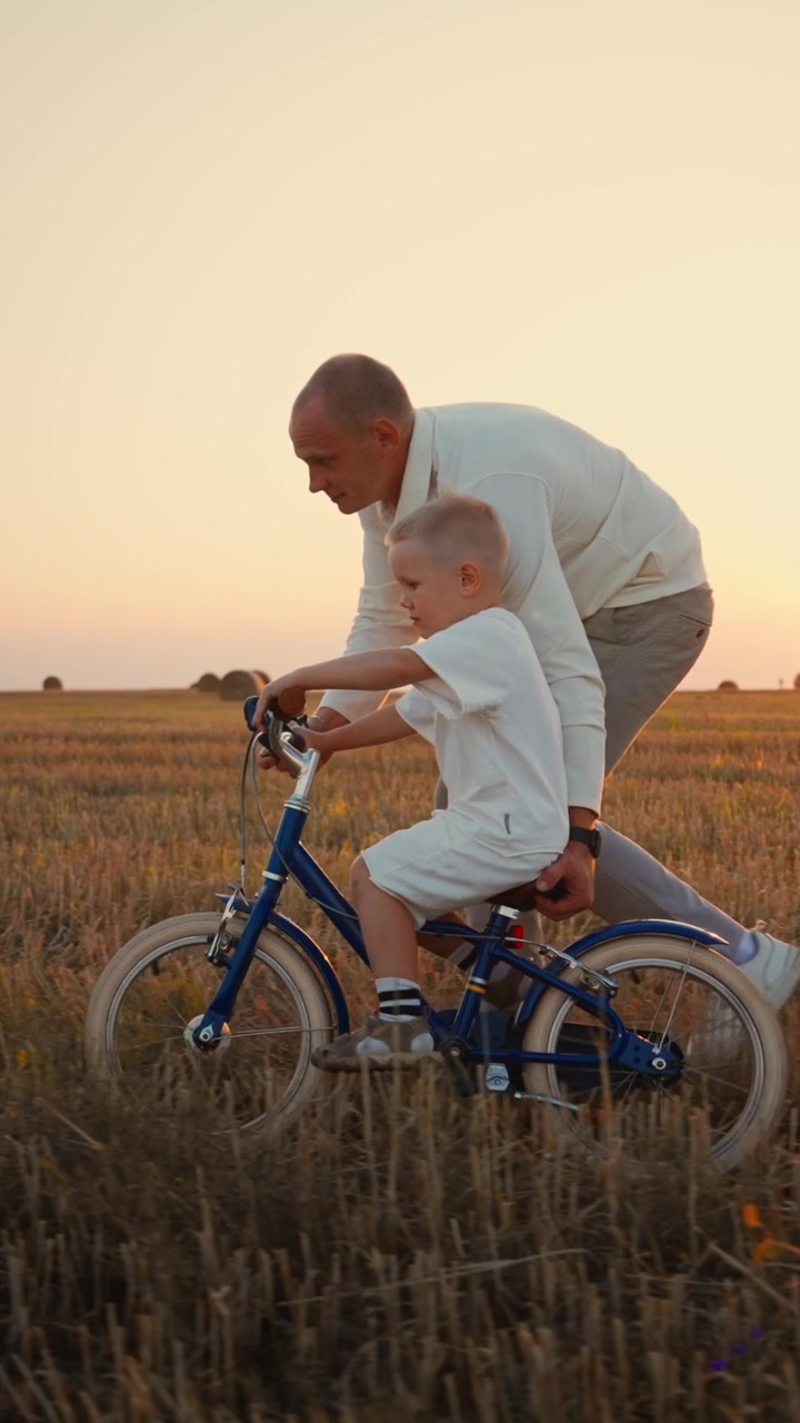 Padre che insegna al figlio piccolo ad andare in bicicletta in un campo al tramonto
